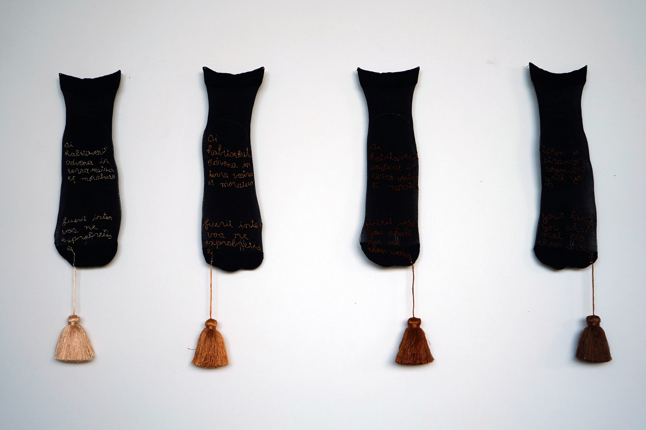 Dirt, Skin and Gold, 2019,Secondhand socks, silk thread embroidery, silk pom poms, 8 x 20 cm each. Socks embroidered with Old Testament text related to rights to land, translated in different ways. 